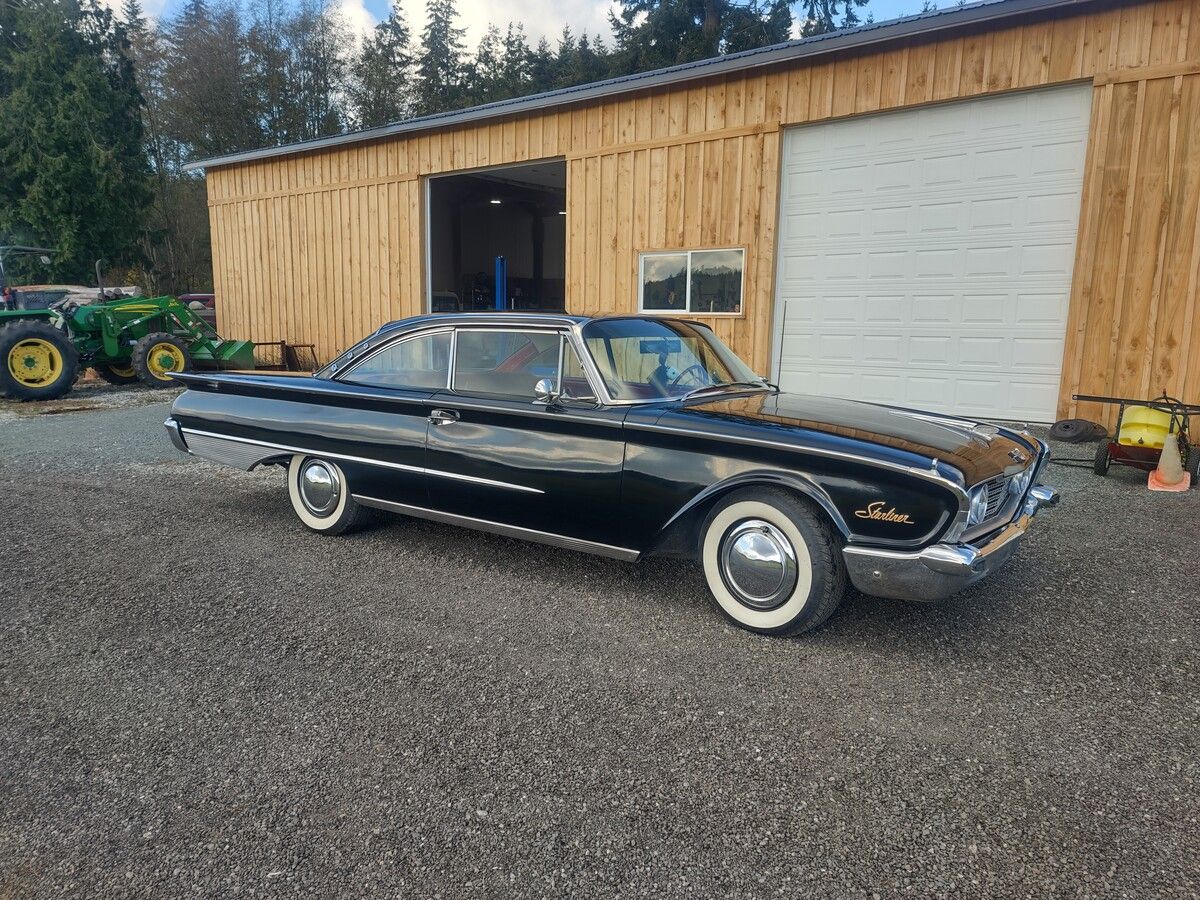 A black car is parked in front of a wooden garage.