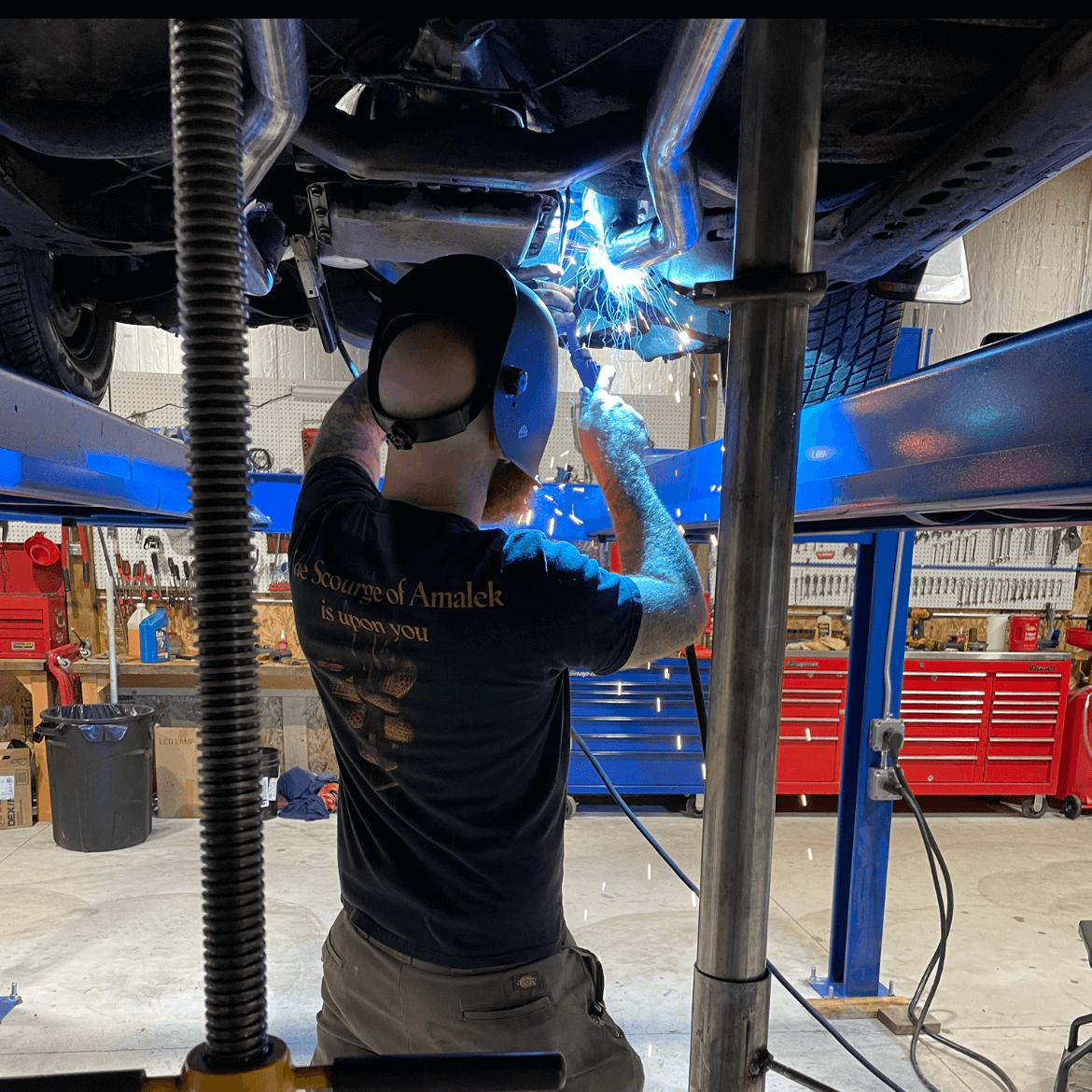 A man is welding under a car in a garage.