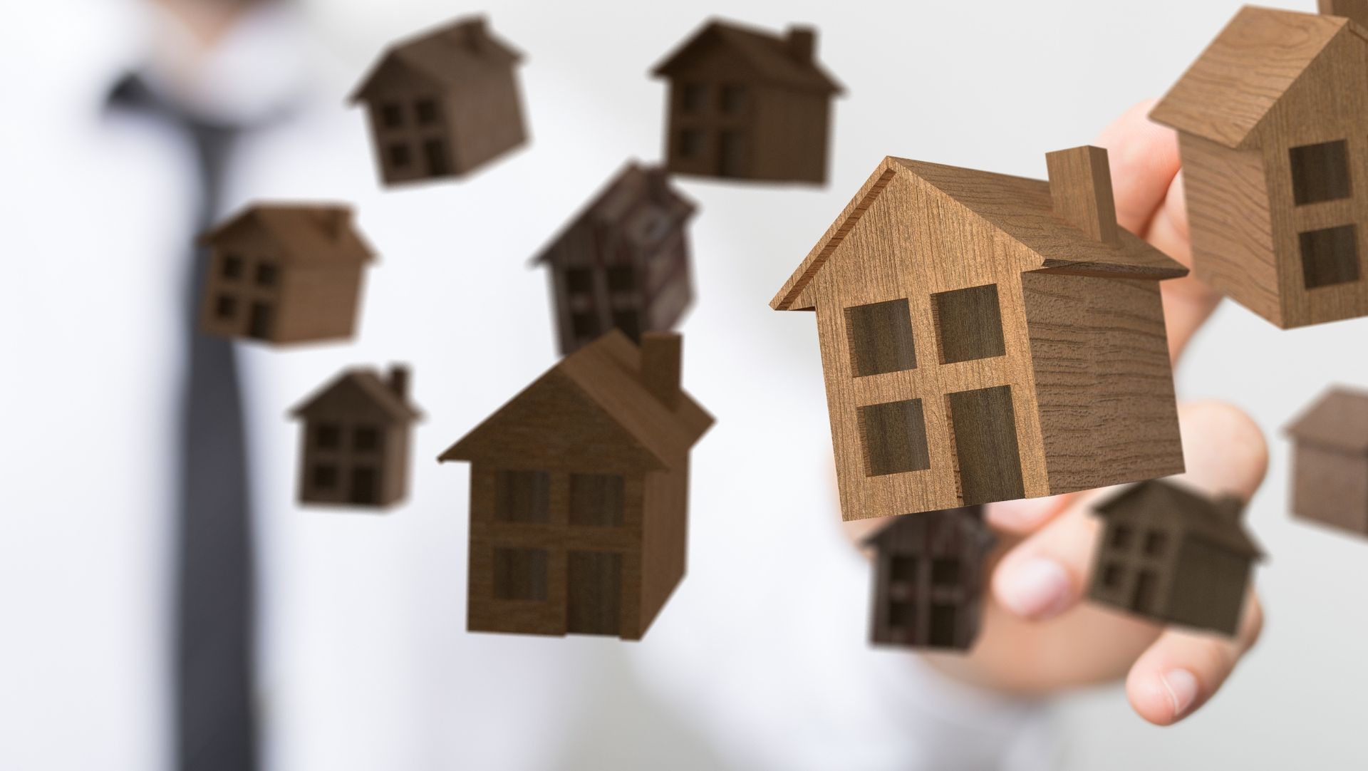 Person in white shirt and black tie pointing at floating wooden house models, representing real estate.