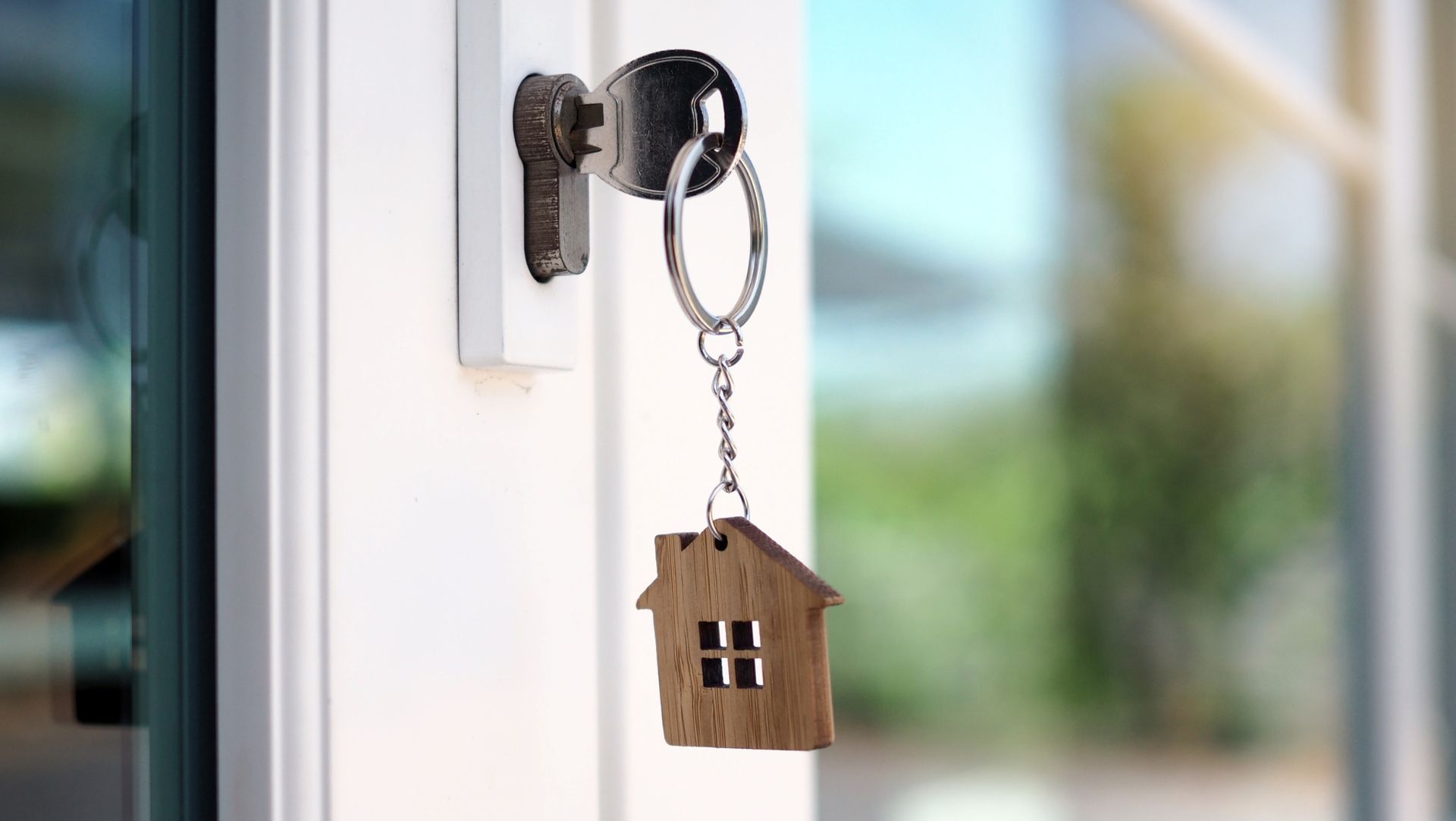 A key with a house-shaped keychain inserted into a door lock, symbolizing home ownership or security.