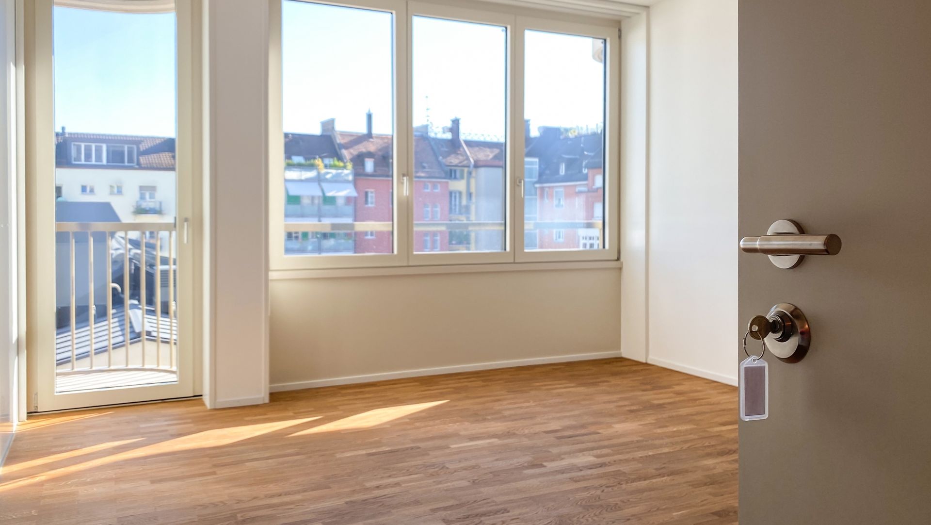 Bright room with wooden floors, large windows, balcony, sunlight, and partially open door on a rental home.
