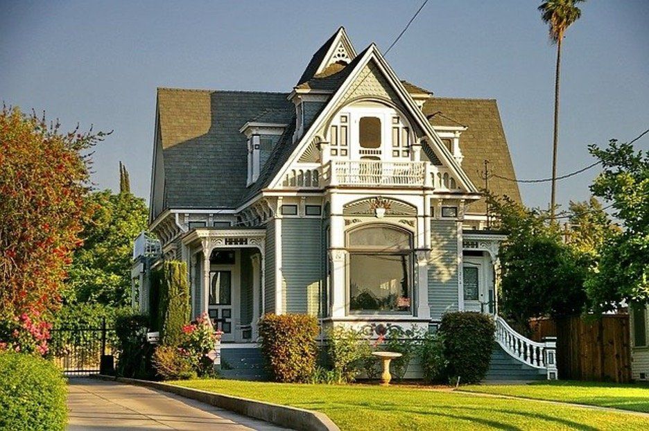 An elegant victorian-style house bathed in warm sunlight, showcasing intricate architectural details and surrounded by a well-manicured lawn.