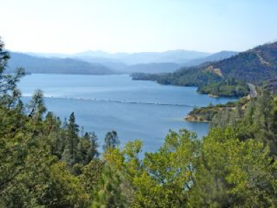 Panoramic view of Whiskeytown Lake, vibrant blue waters surrounded by rolling wooded hills under clear blue sky.