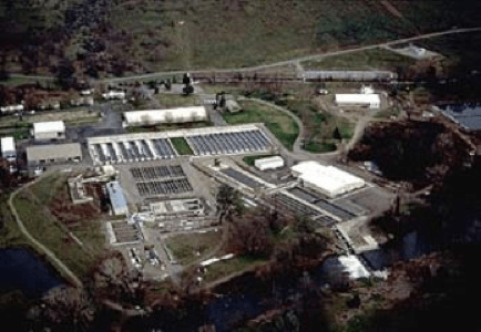 Aerial view of Coleman Fish Hatchery, water treatment facility with multiple buildings, surrounded by green patches, road, clear skies.