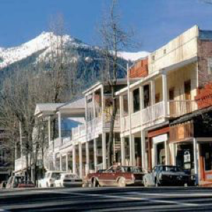 Picturesque street view with row of two-story buildings, balconies, old-fashioned architectural style, snow-capped mountain in background.