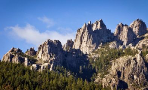 Castle Crags - Rugged mountain peaks, jagged rock formations against clear blue sky, pine trees at lower elevations.
