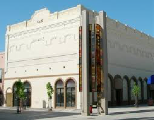 Historic two-story theater building with white facades, arch windows, vertical neon sign on sunny day.