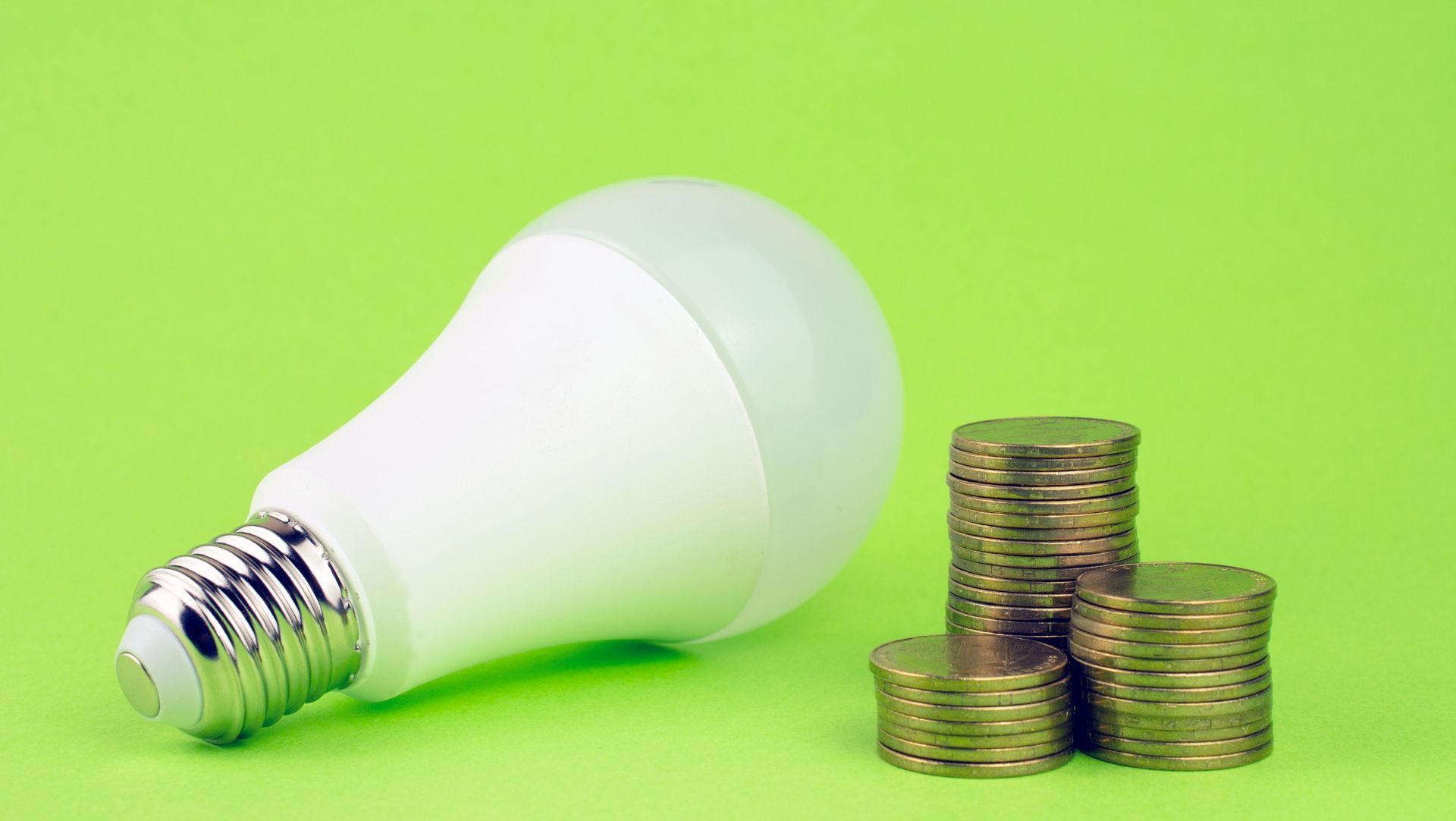 Compact fluorescent bulb next to a stack of gold coins. 