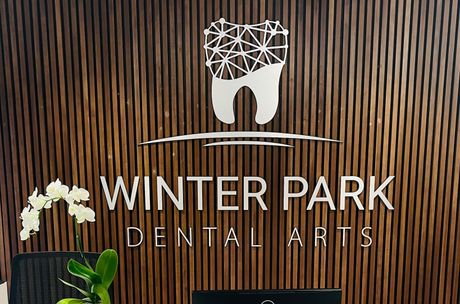 A sign for winter park dental arts is on a wooden wall.