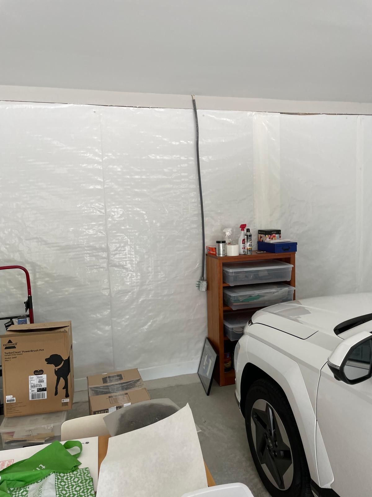 A white car is parked in a garage under a white tarp.