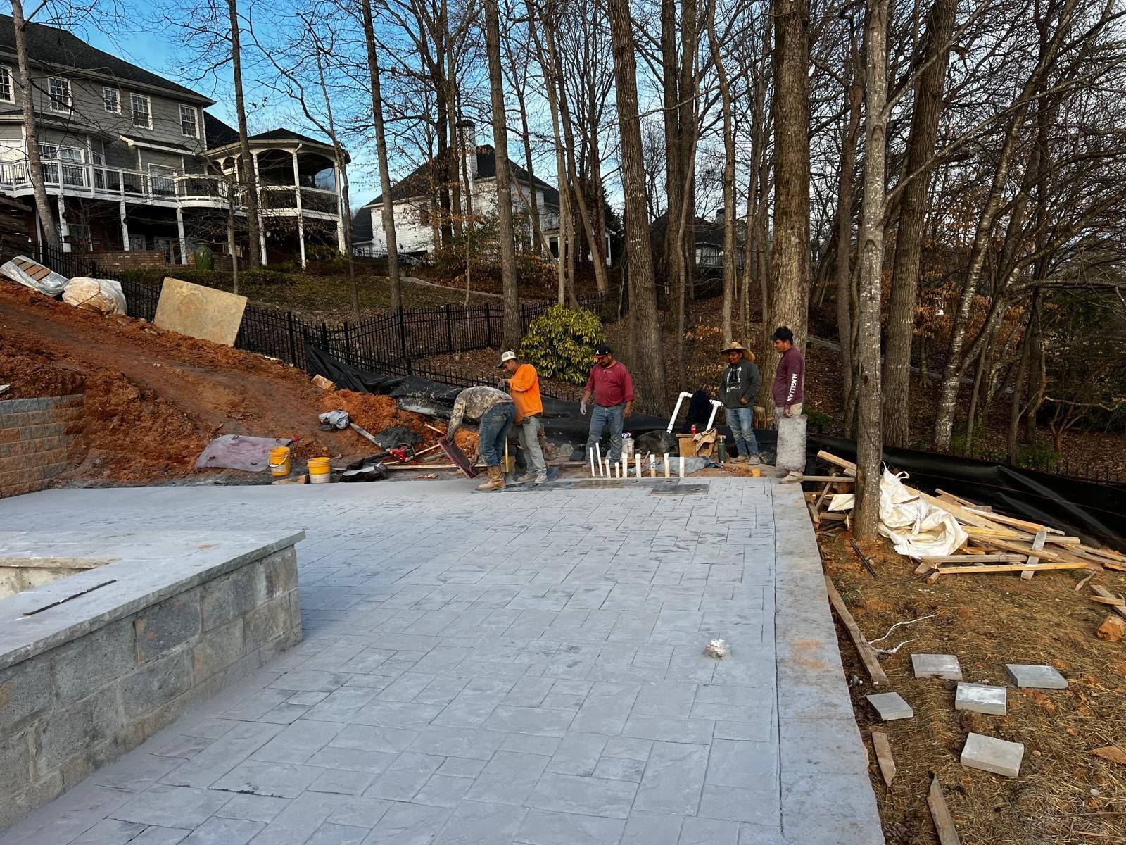 A group of construction workers are working on a concrete floor in front of a house.