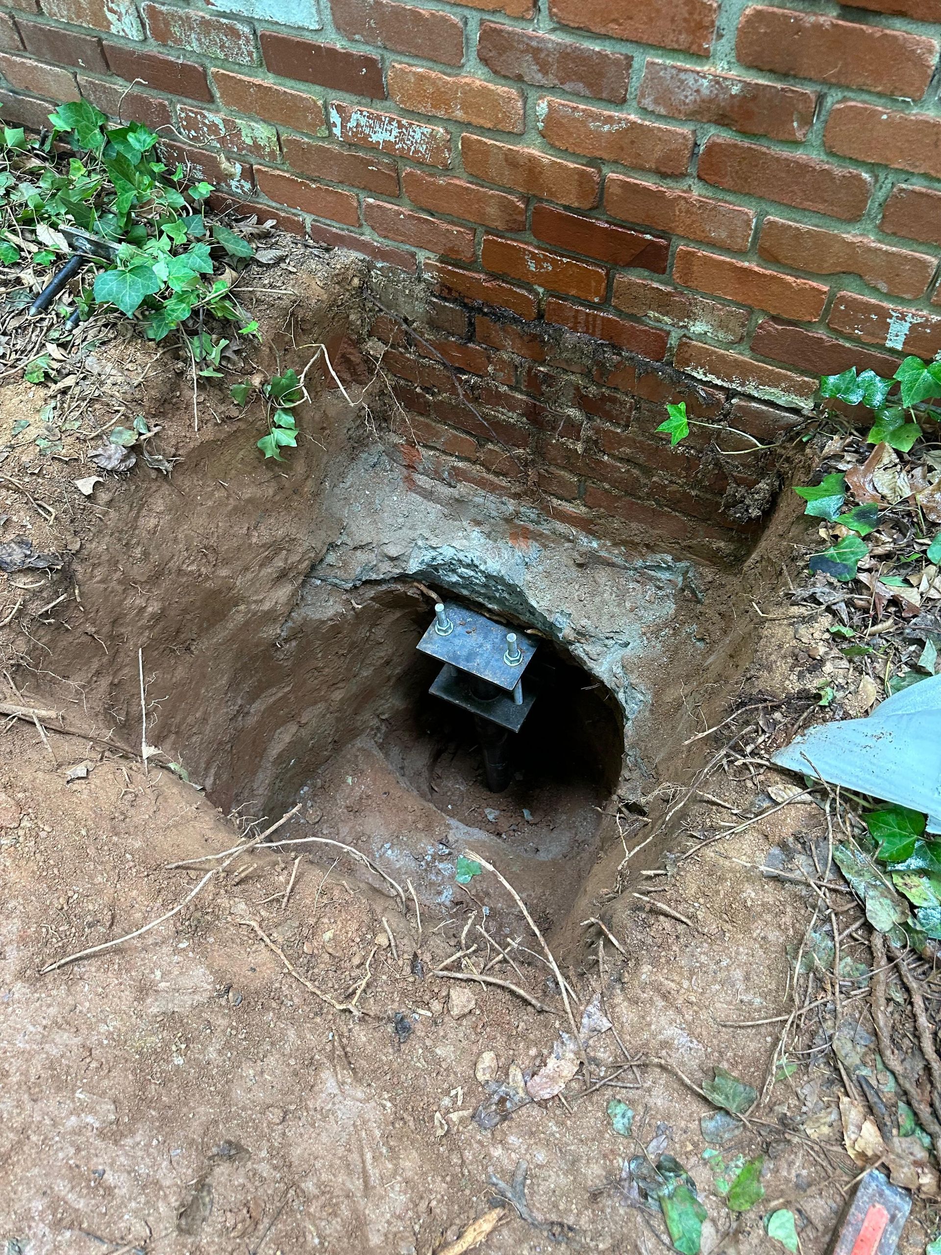 A hole in the ground next to a brick wall.