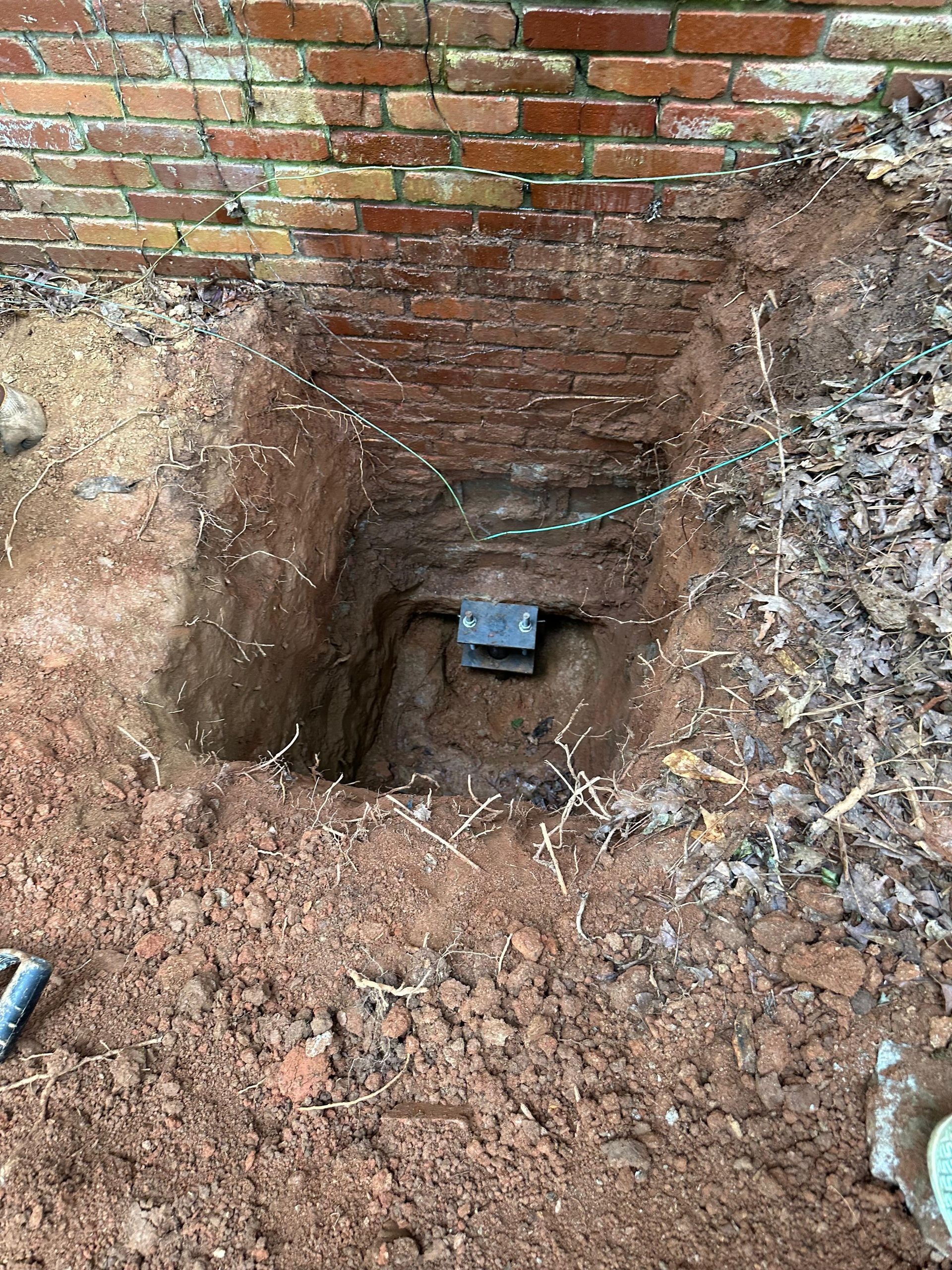 A hole in the ground next to a brick wall with a box in it.