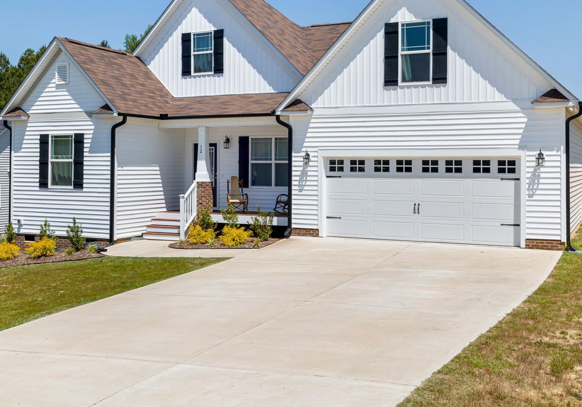 A large white house with black shutters and a concrete driveway.