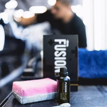 A person is applying a coating to a red car.