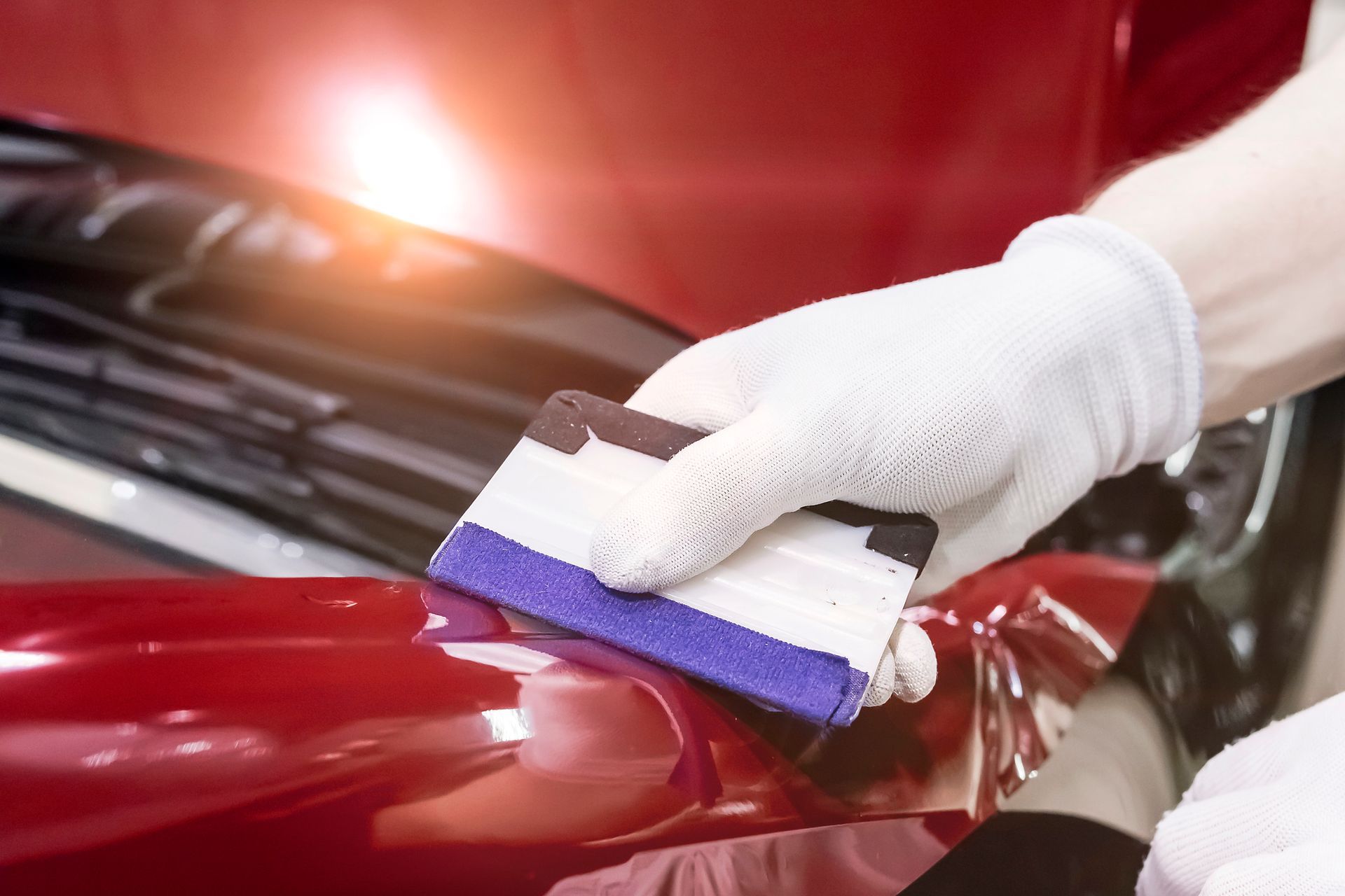 A person is wrapping a red car with a squeegee.