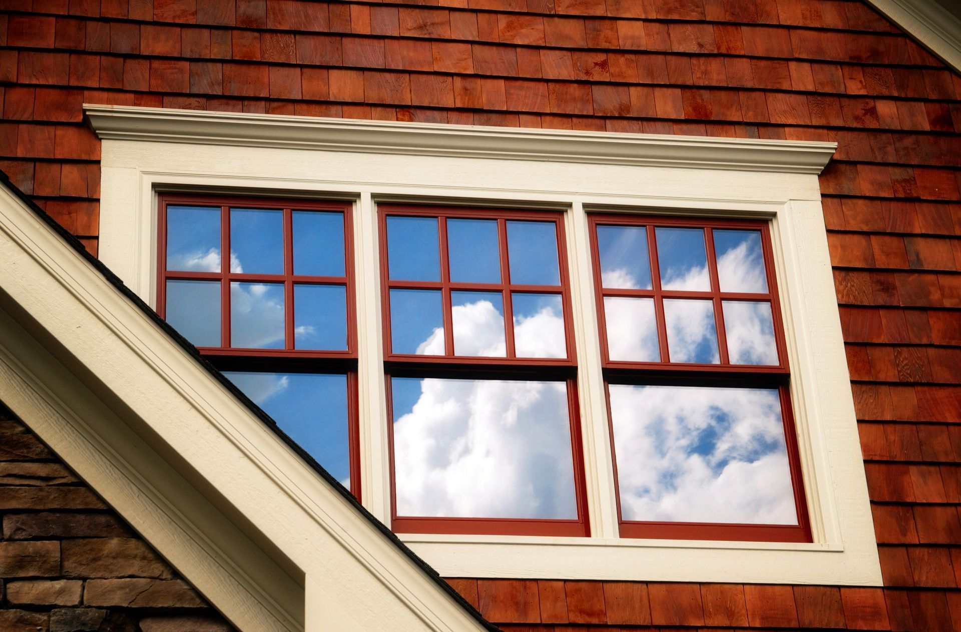 A window on the side of a house with a cloudy sky reflected in it