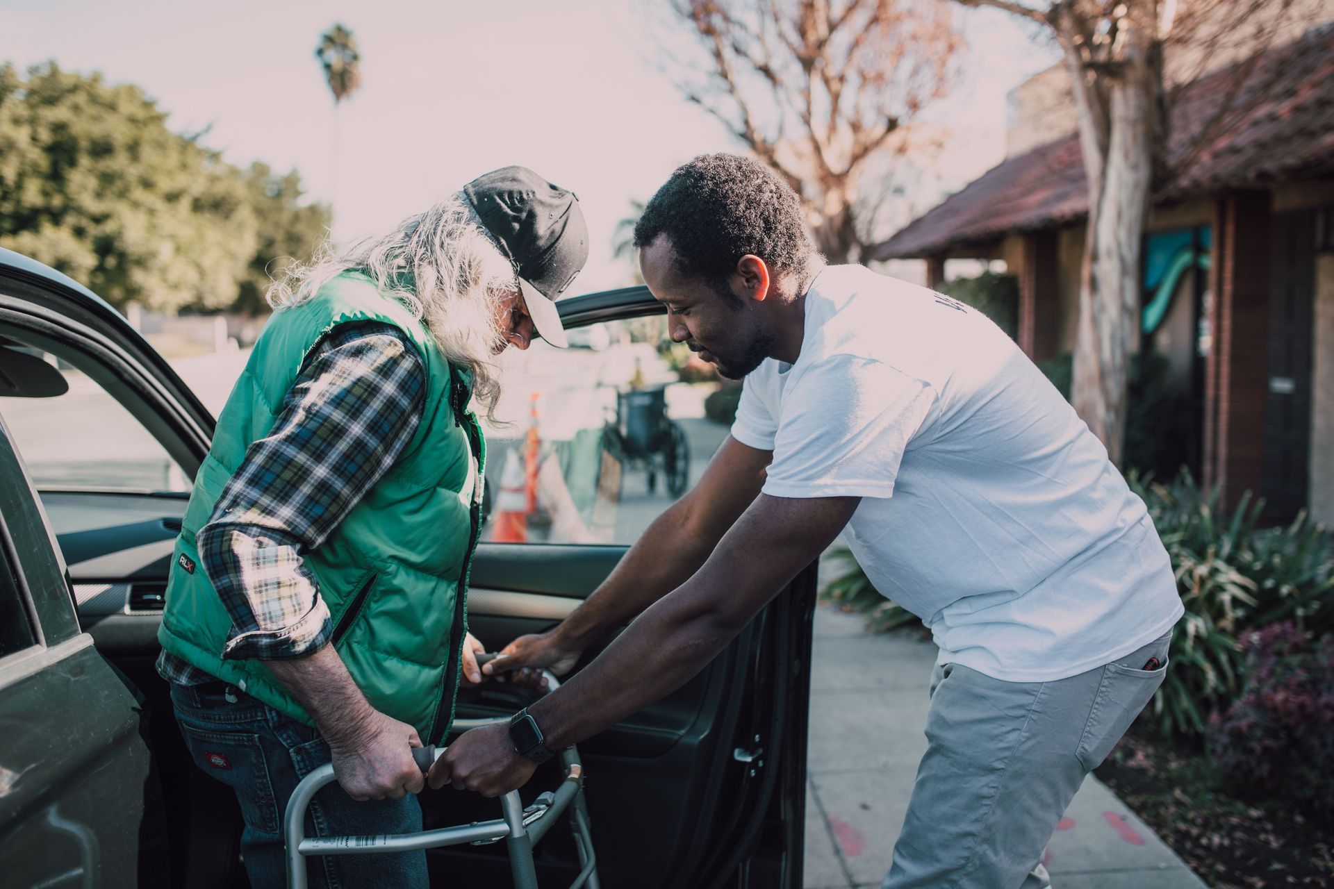 Two people helping a seated person into a car outside a house