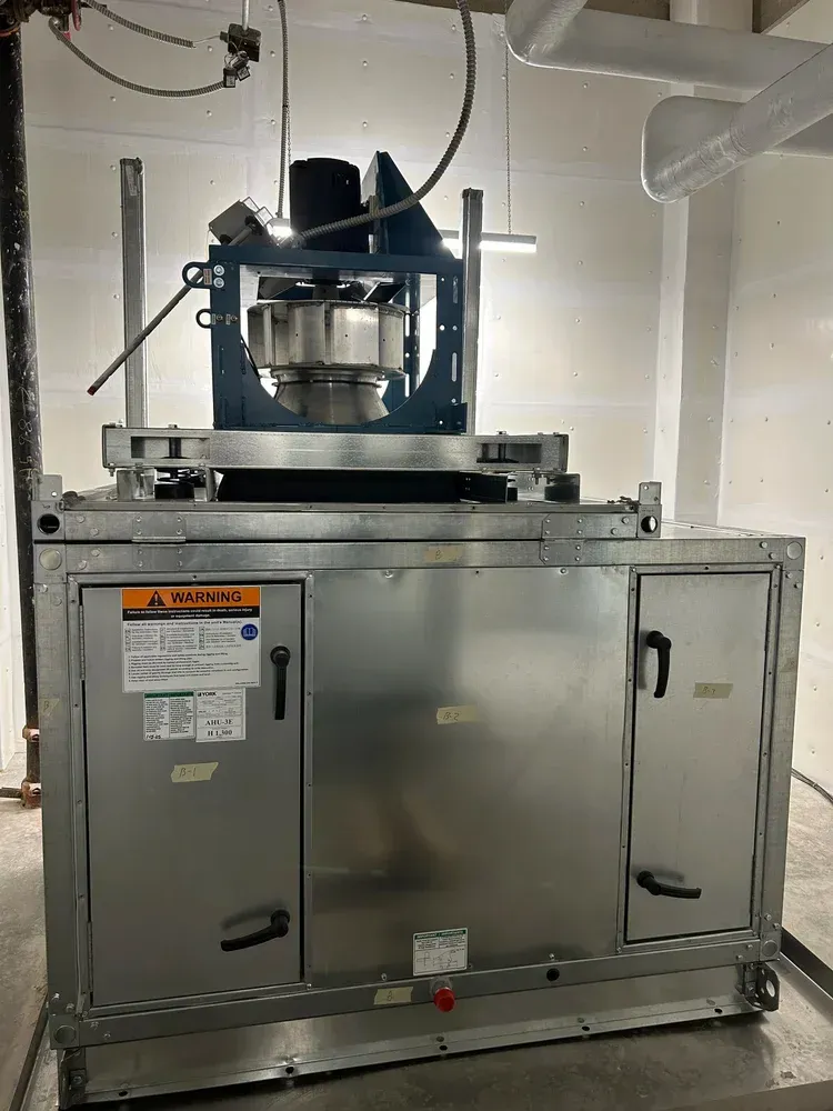 Stainless steel industrial machine with a central rotating assembly, set against a white wall in a workshop.