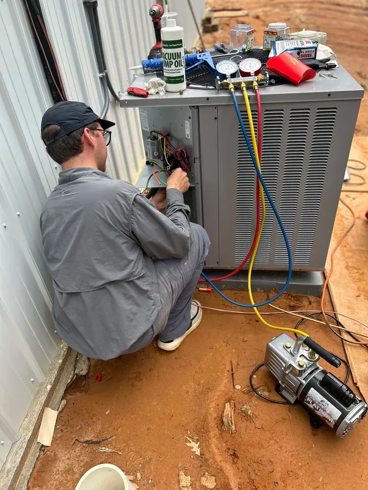 Technician servicing an outdoor HVAC unit with gauges and tools on the ground.