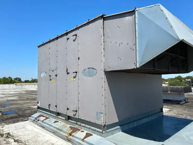 Large gray rooftop HVAC unit with a ducted vent on a flat roof under a blue sky