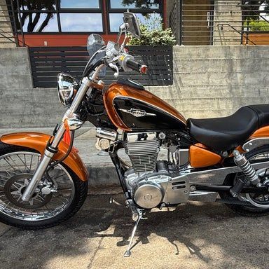 Orange and black motorcycle parked on a sidewalk in front of a building.