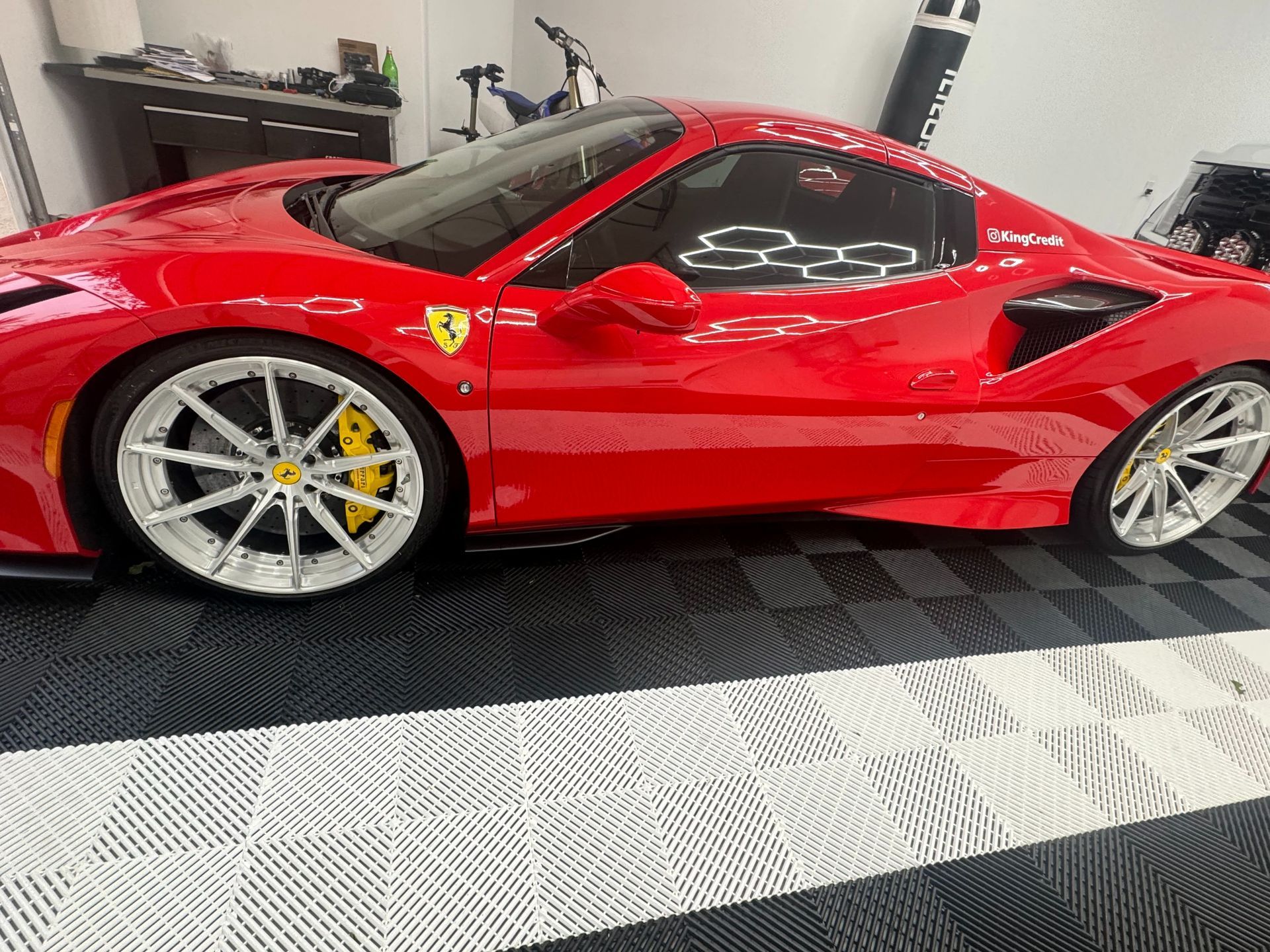 Red Ferrari with white rims and yellow calipers parked on a black and white tiled floor.