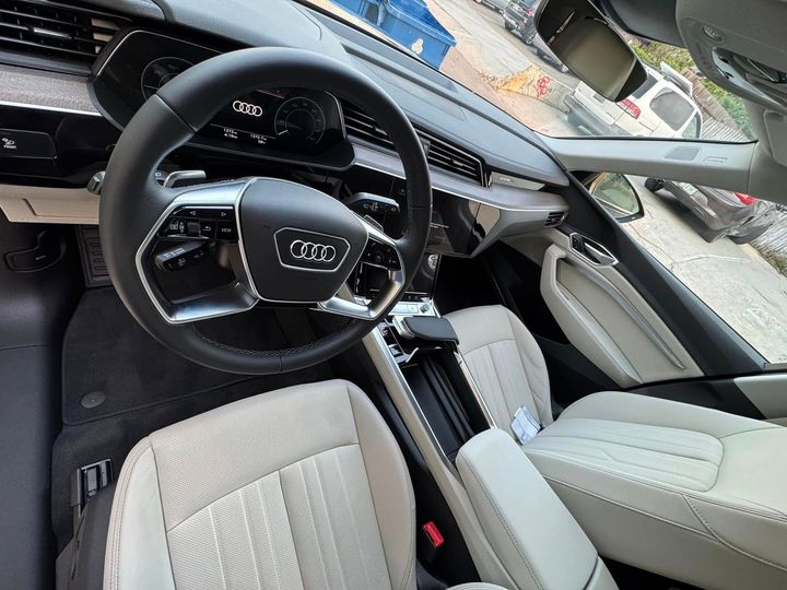 Interior view of an Audi, showing the steering wheel, dashboard, seats, and console; light-colored upholstery.