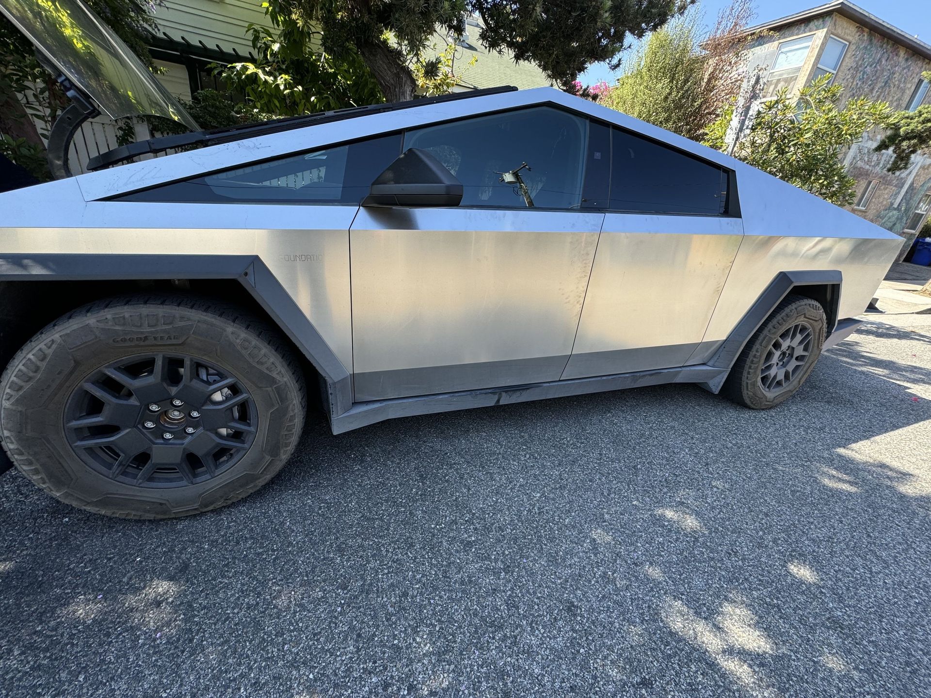 Tesla Cybertruck, silver, parked on gravel, partially visible side profile.