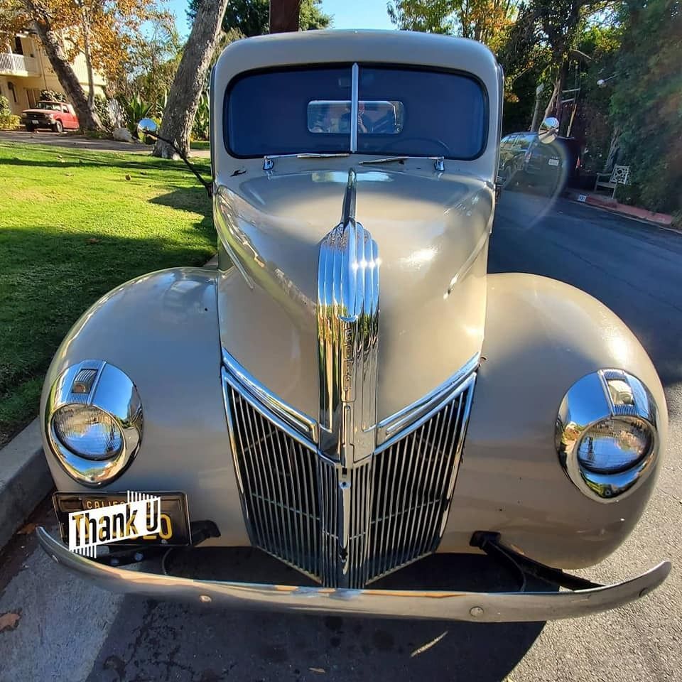 Tan 1939 Ford coupe parked on the street with chrome grill and headlights.