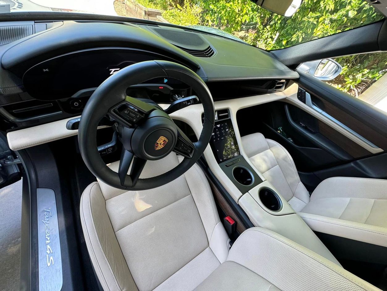 Interior of a cream and black Porsche Taycan. Steering wheel, seats, and dashboard are visible.