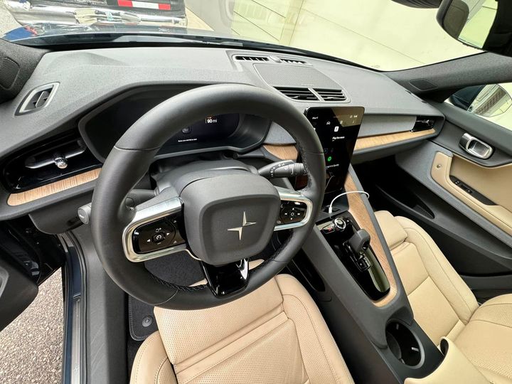 Interior of a Polestar electric car: steering wheel, dashboard, tan leather seats, wood trim, and a central touchscreen.