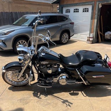 Black Harley-Davidson motorcycle parked on a paved driveway; a silver SUV and garage are in the background.