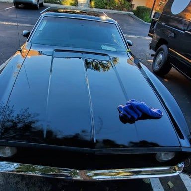 Black classic car hood with a blue cloth in a parking lot.