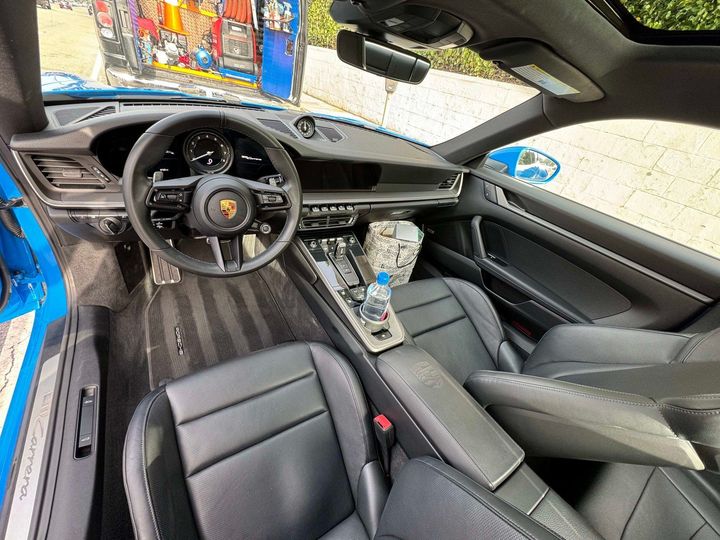 Interior of a blue Porsche sports car with black leather seats, steering wheel, and dashboard.