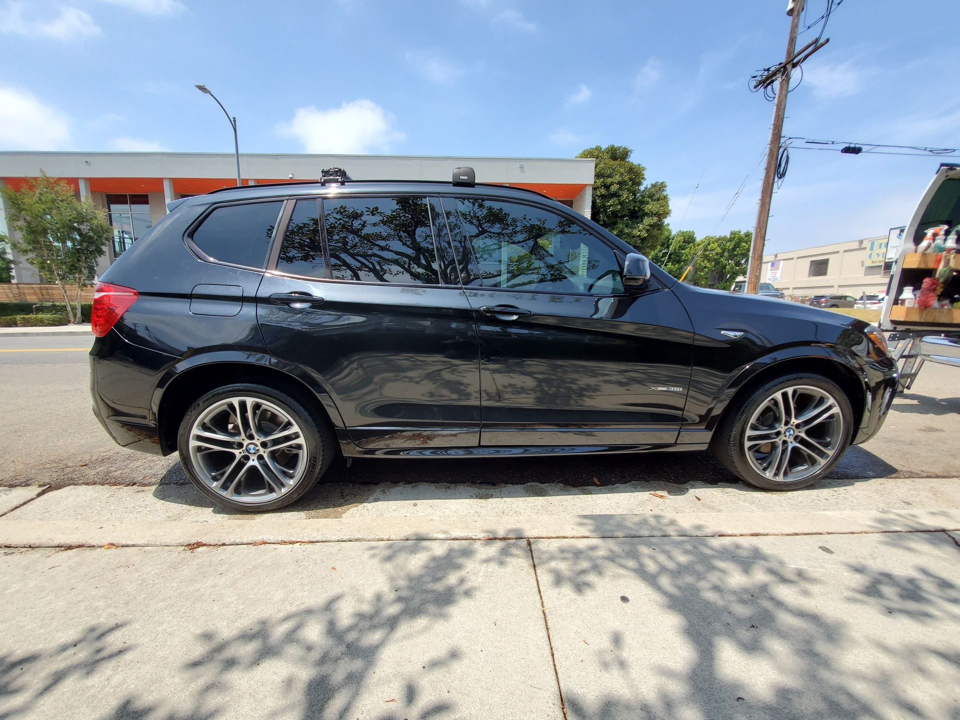 Black BMW SUV parked on a sidewalk. The car is black, with tinted windows and silver rims, in front of a building.