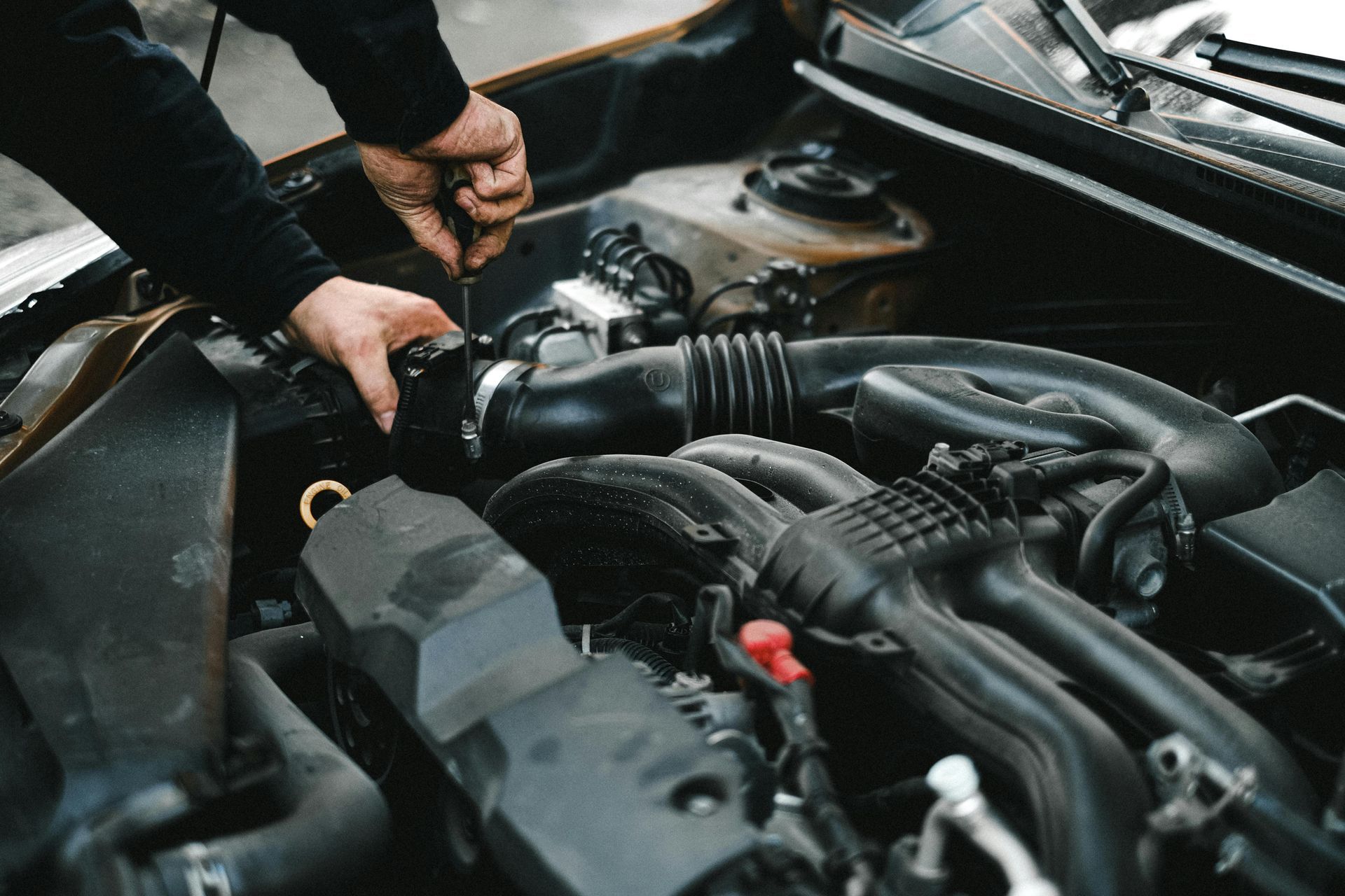 Mechanic working on a car engine, using a tool, in a garage setting.