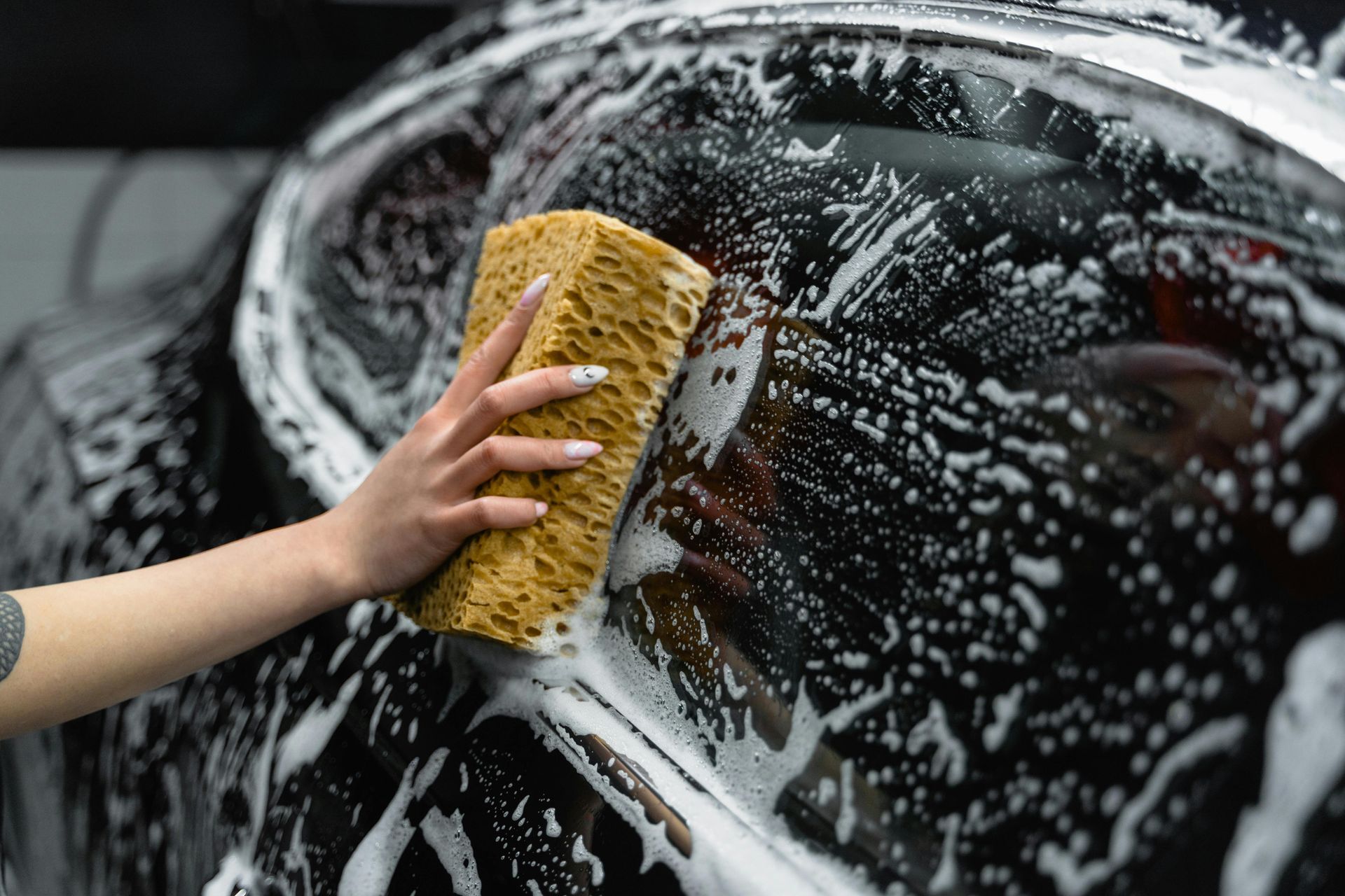 Hand washing a black car with a soapy sponge.