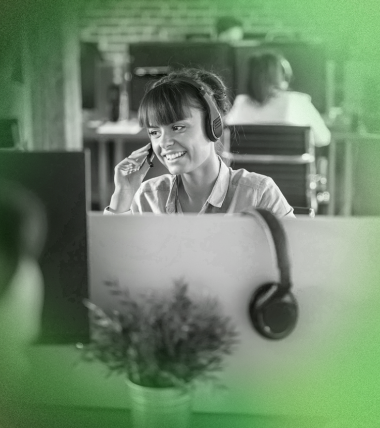 Woman wearing headset smiles, working at a desk in a call center.