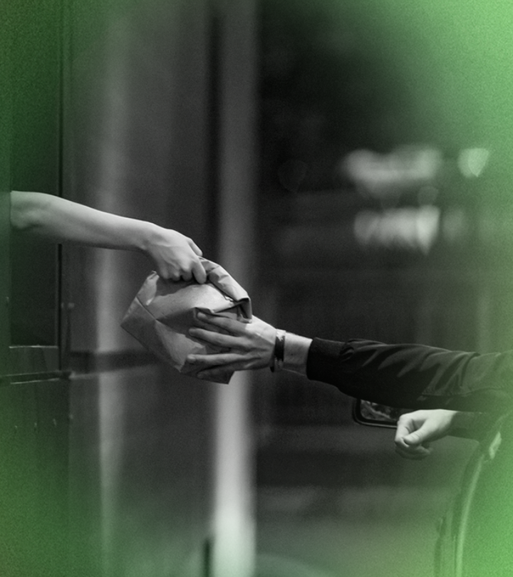 Hands exchanging a folded paper package from a car window, grayscale image.