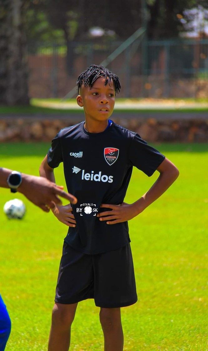 A young boy is standing on a soccer field with his hands on his hips.