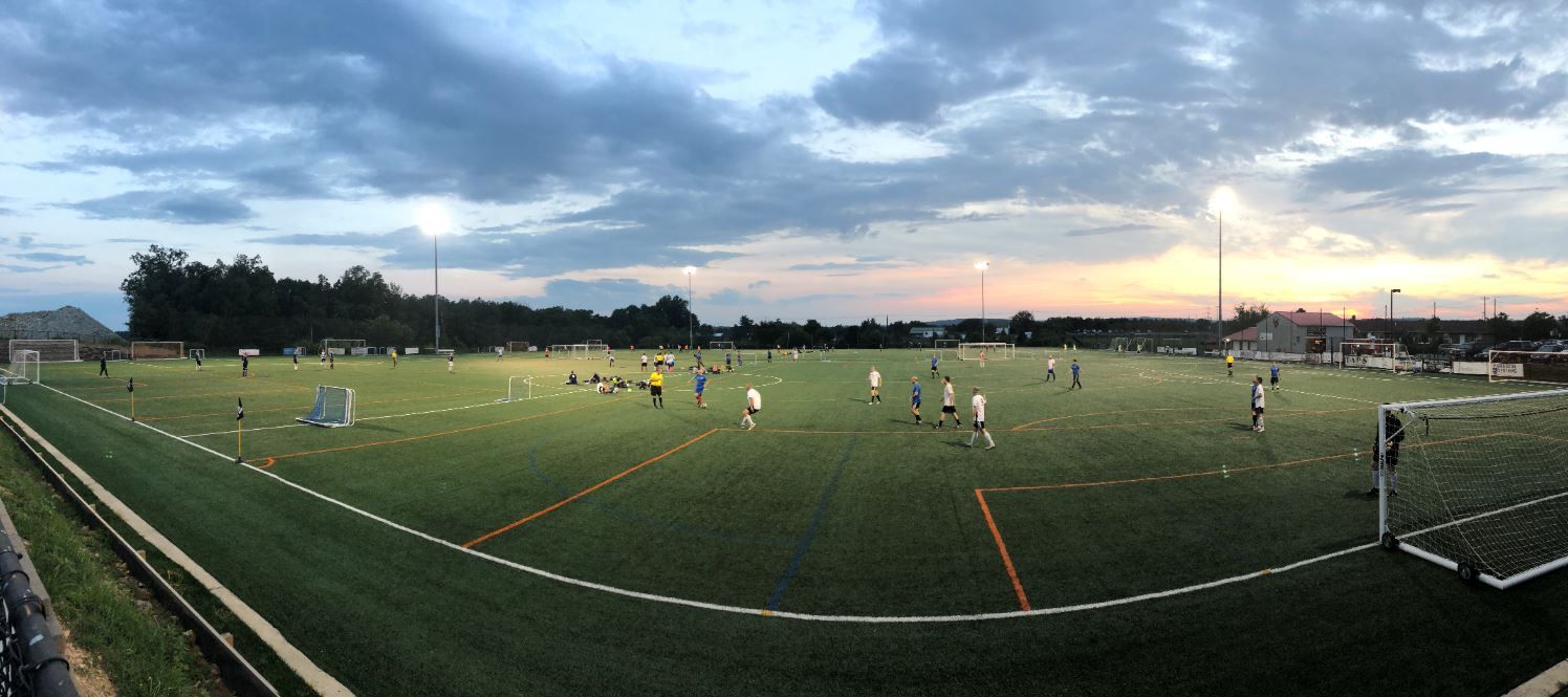 A group of Loudoun Soccer players playing soccer on a field at sunset.