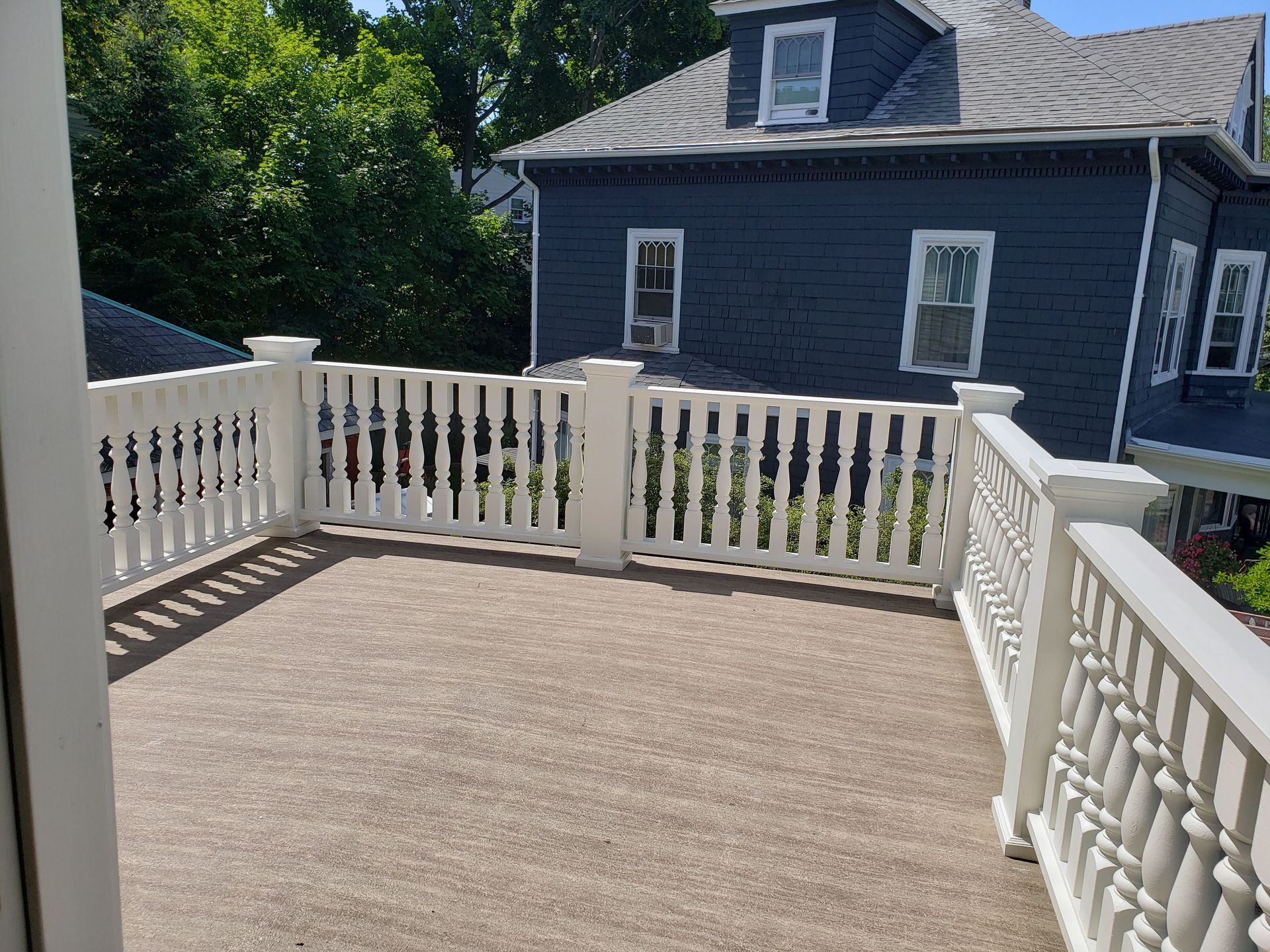 White-railed deck overlooks a blue house and trees on a sunny day.