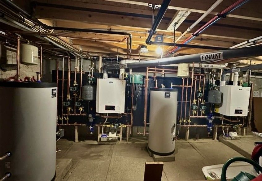 Basement mechanical room with multiple water heaters, boilers, and copper piping.
