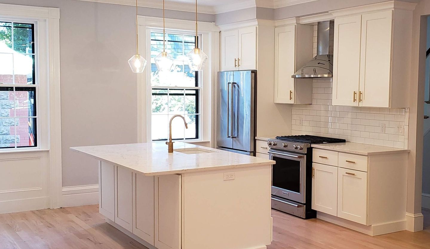 Bright kitchen with white cabinets, island, and countertops; stainless steel appliances, light wood floors.