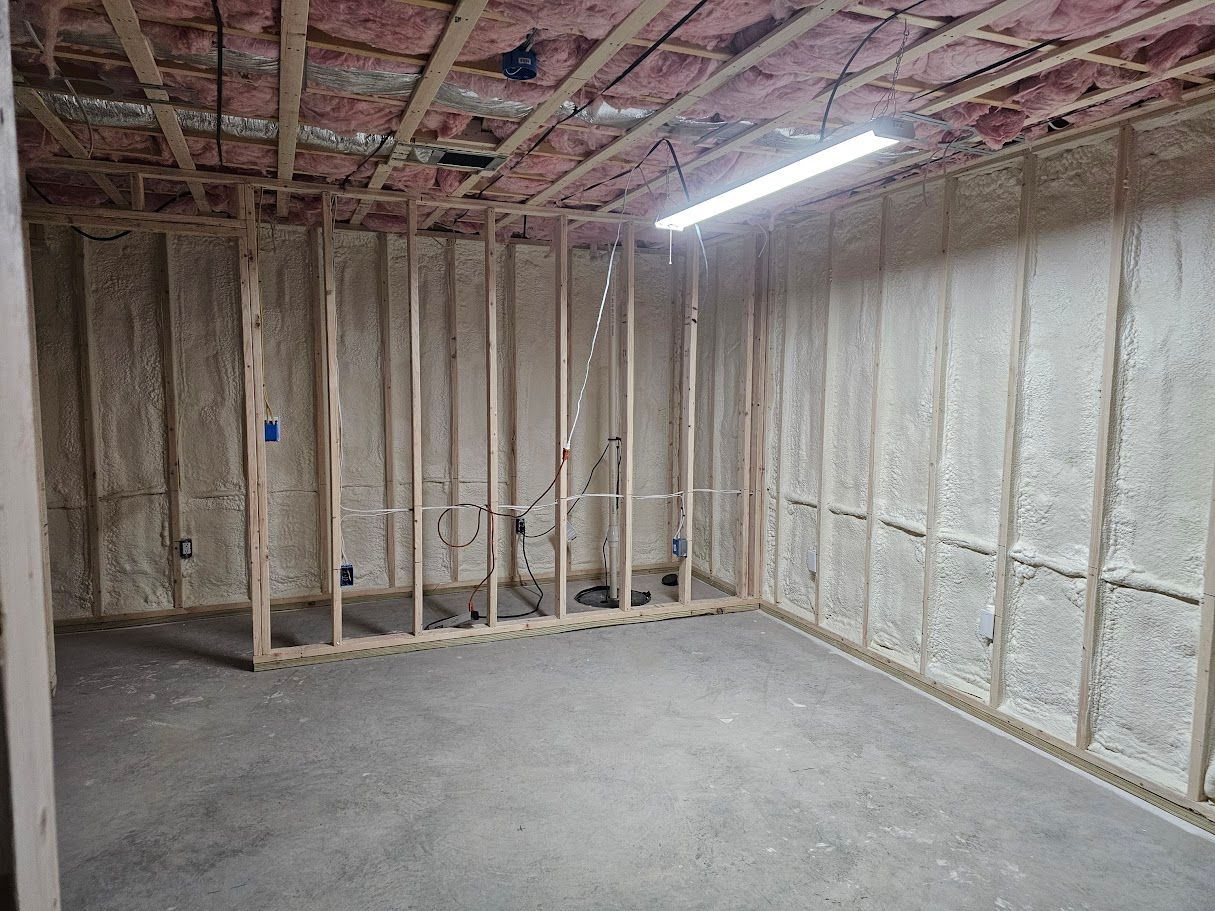 Interior room with wooden framing, spray foam insulation, concrete floor, and a fluorescent light.