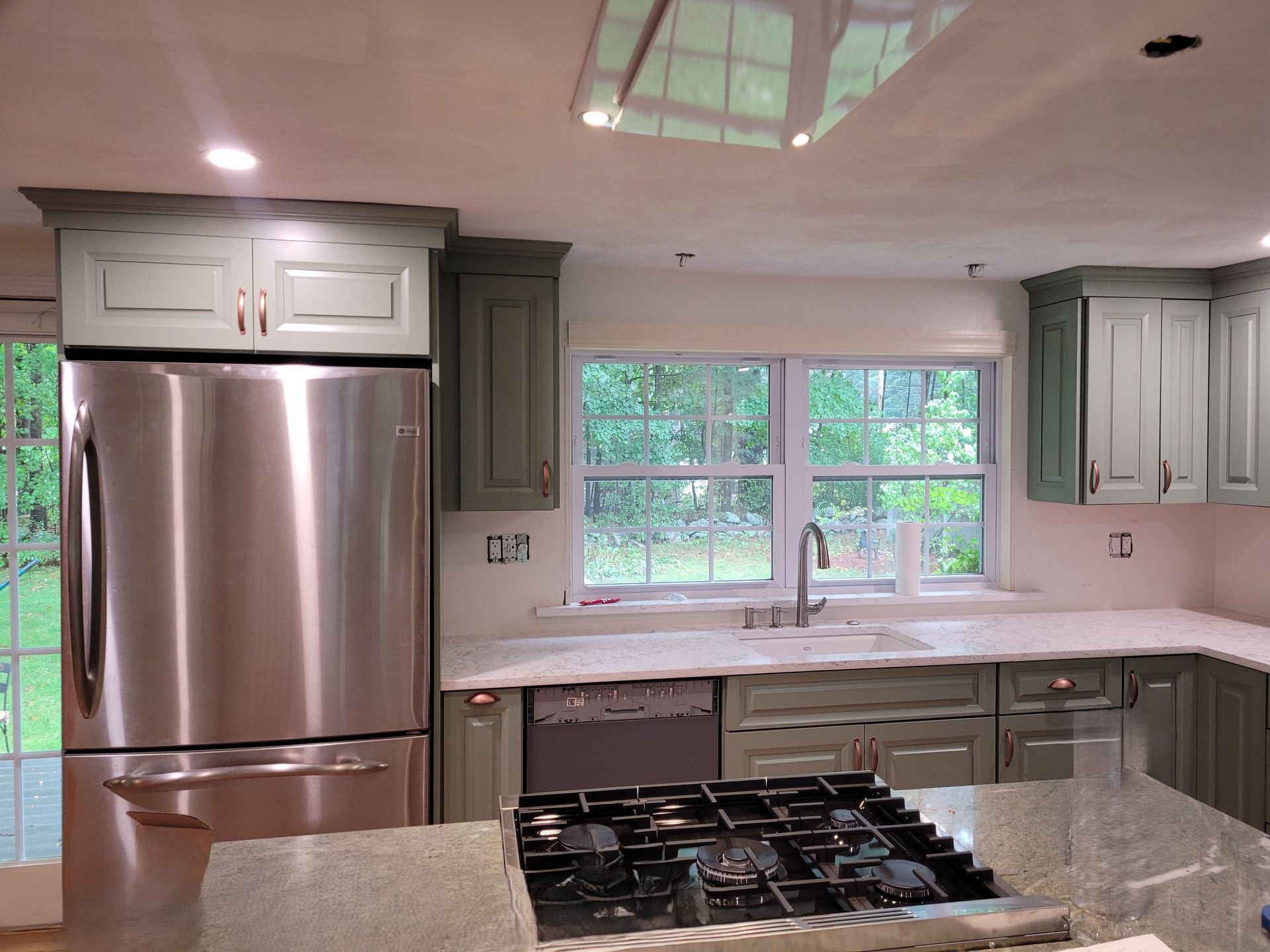 Bright kitchen with white cabinets, island, and countertops; stainless steel appliances, light wood floors.