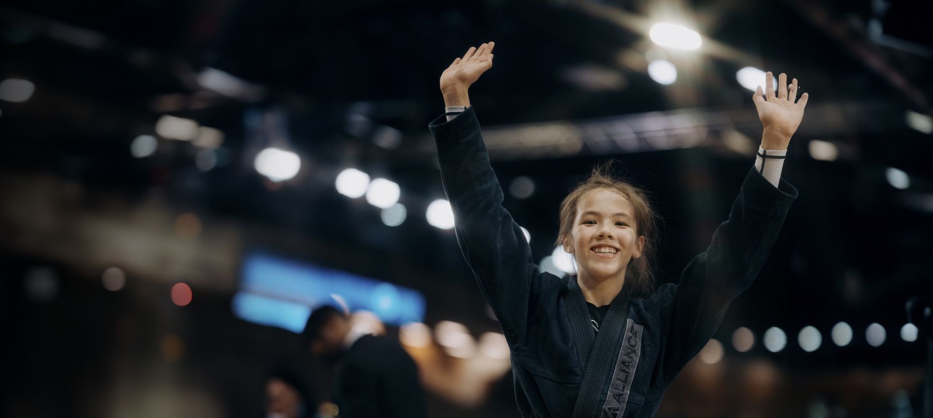 A young girl is standing in a dark room with her arms in the air.