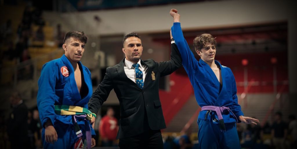 A referee is standing between two wrestlers in a wrestling match.
