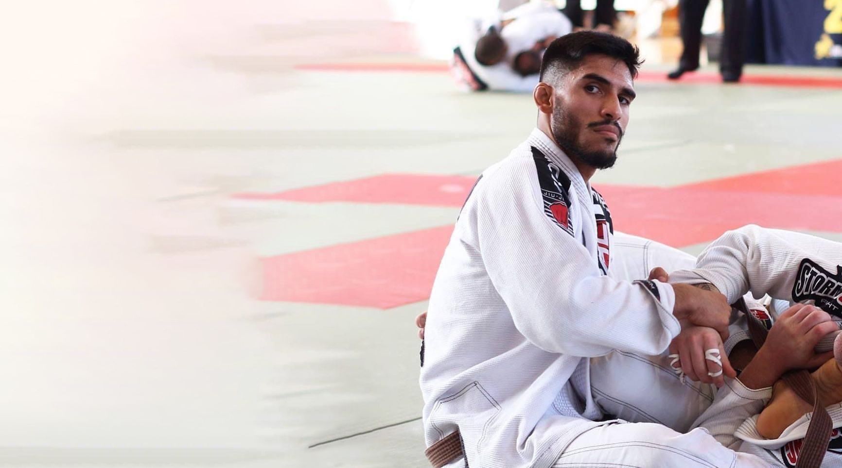 A man in a white kimono is sitting on a judo mat.